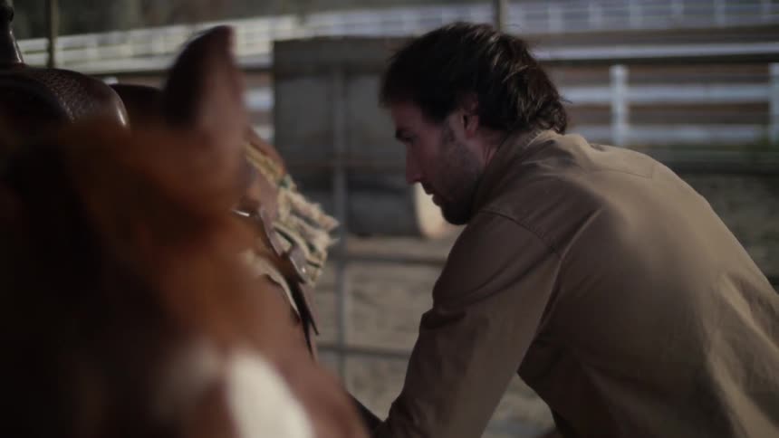 A man adjusts a saddle on a horse