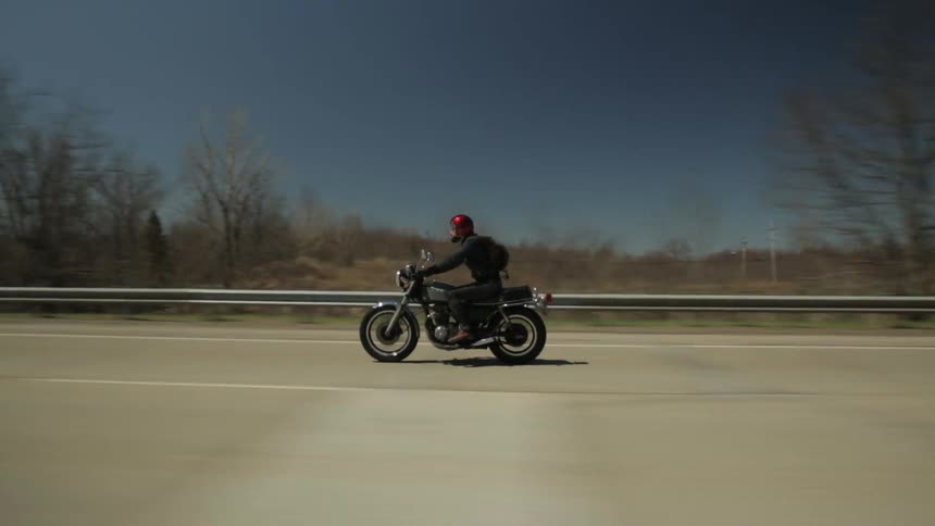 A man riding a motorcycle down the highway is passed by a silver sedan