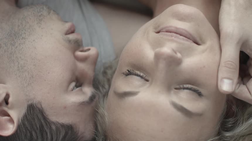 A man stroking a woman's face and playing with her hair as they lay next to each other and relax