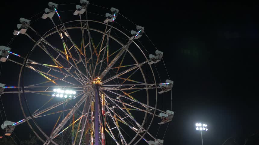 An empty ferris wheel sits with its decorating lights flash and animate