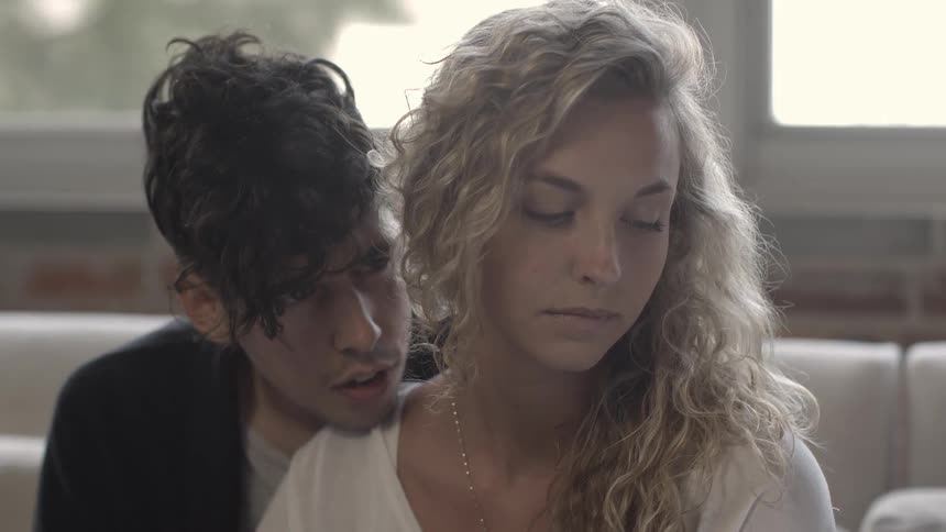 A man is snuggled up to a woman talking, and then kissing her neck