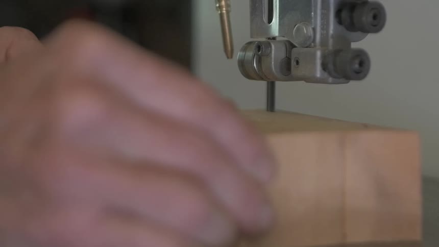 A person cuts a block of wood with a band saw