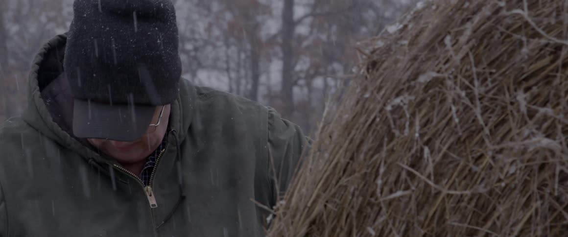 Man working with hay while it snows