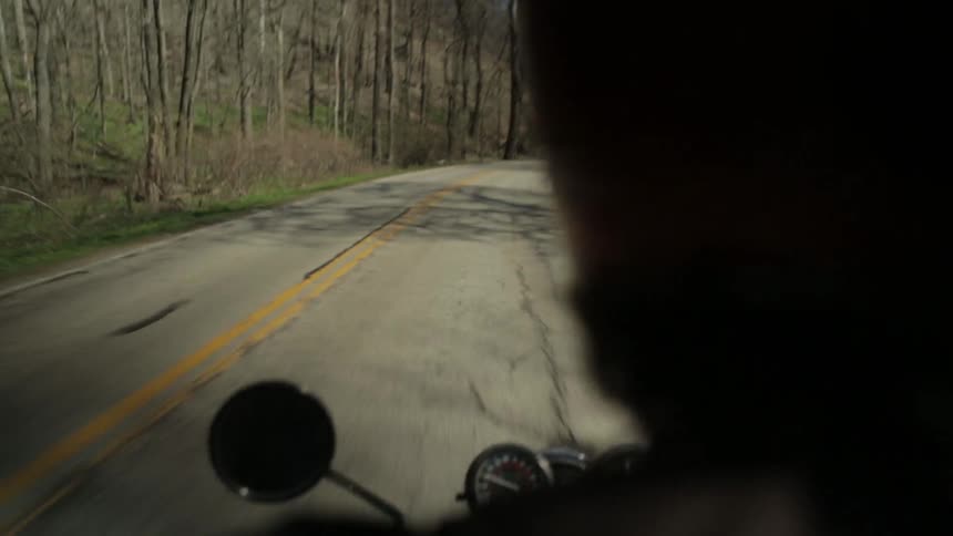 A man motorcycles down a tree-lined road