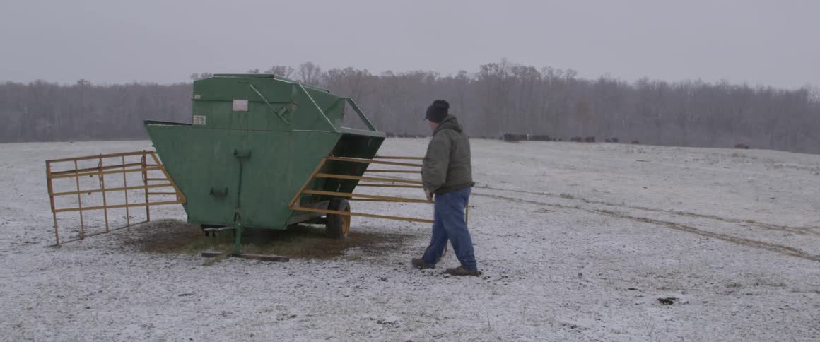 A man walks up to a piece of farm equipment in the snow