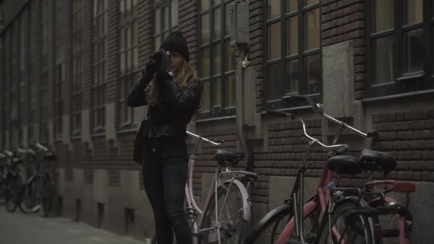 A woman stands near bicycles and takes pictures with a camera