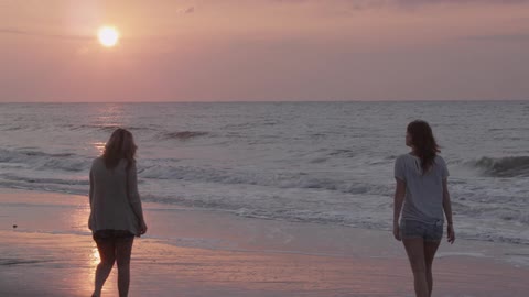 Three women walk on beach near surf near sunset