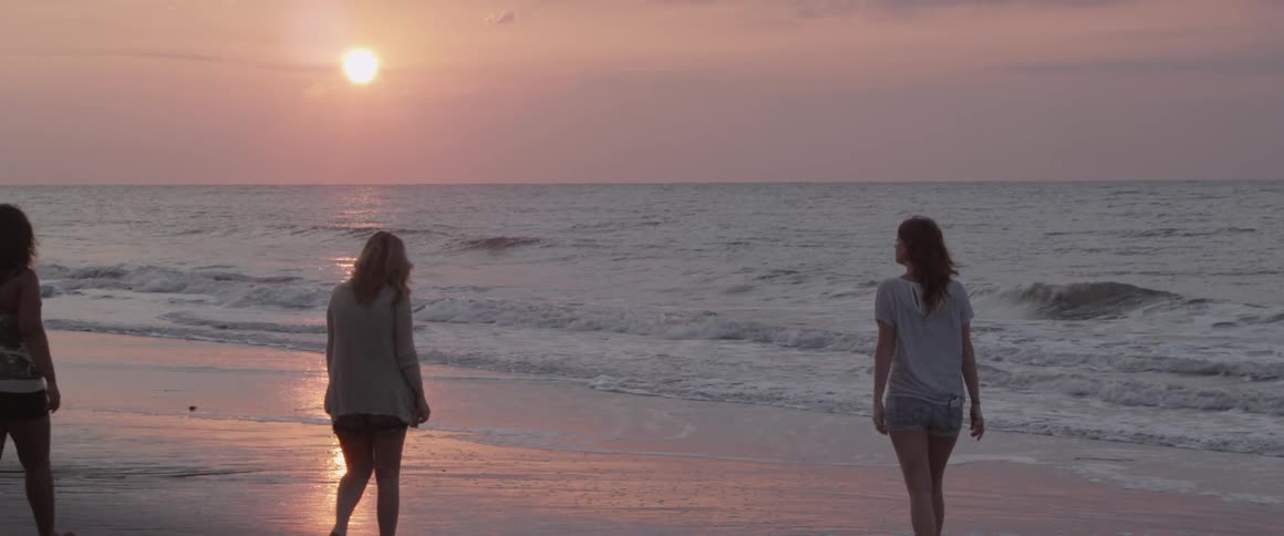 Three women walk on beach near surf near sunset