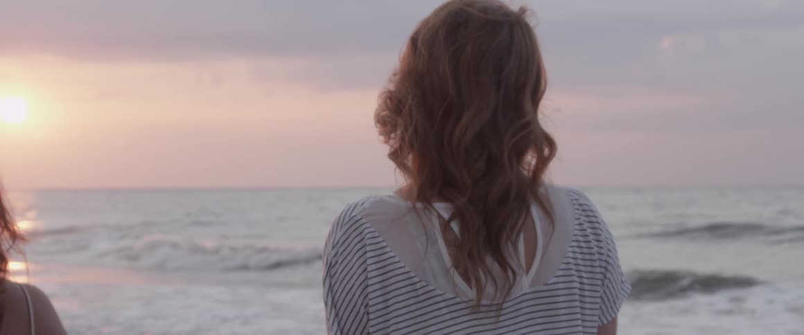 Three women walk towards the ocean at sunset