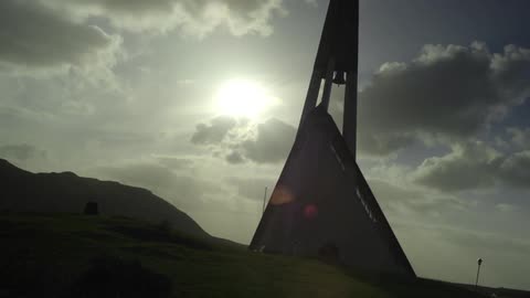 A tall triangular bell tower has a cross at the top