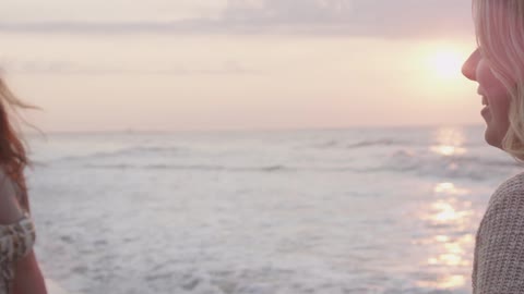 Two women talk and laugh on a beach at dusk