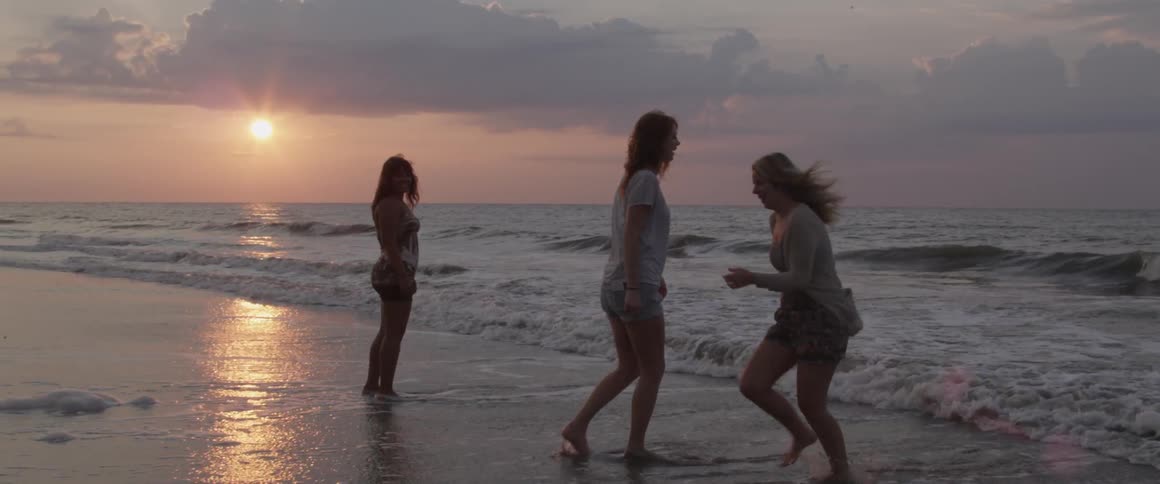 Three women wade in the ocean at sunset