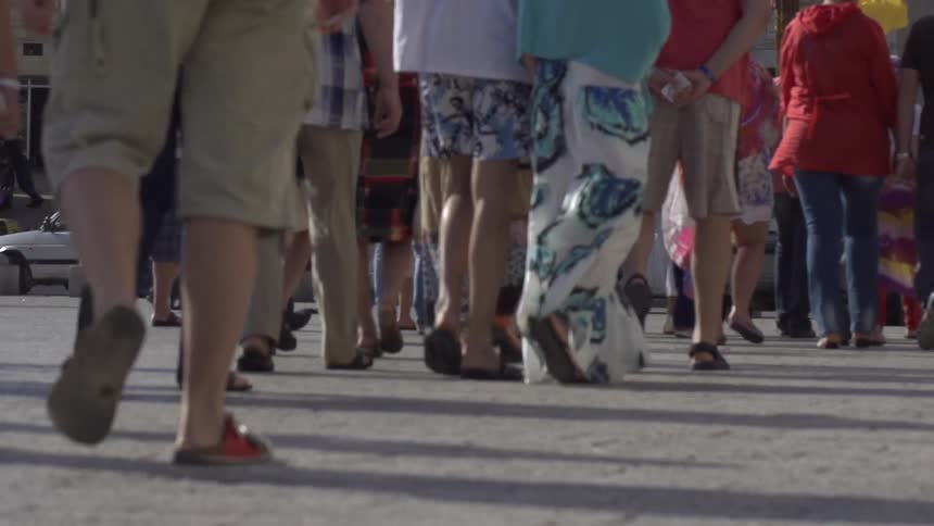 The legs and lower bodies of many people walking on a street