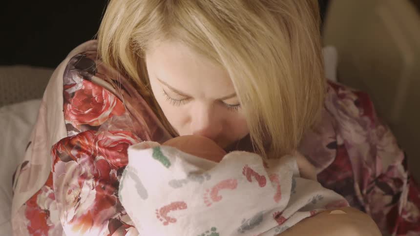 A mother smiling at and kissing her newborn baby