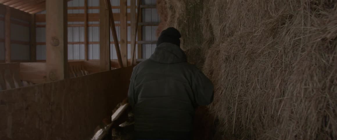 Man walking next to stacks of hay in a barn