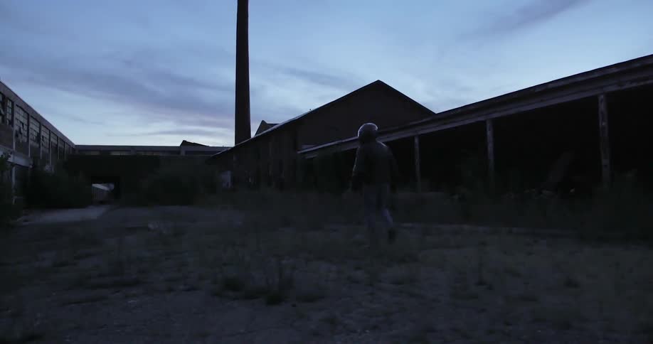 Man in a helmet walking toward an old building at dusk