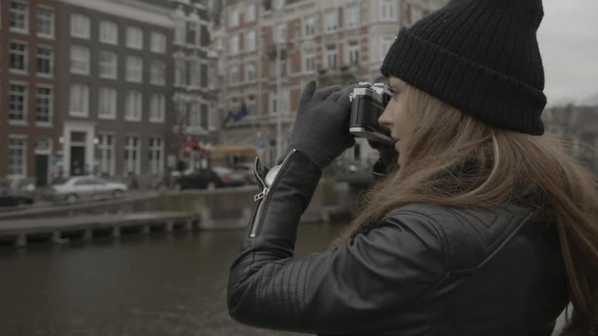 A woman walks along a city canal and snaps a photo