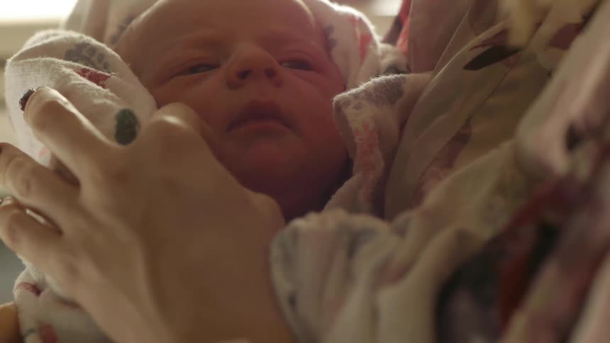 A mother holding and caressing the cheek of her newborn baby