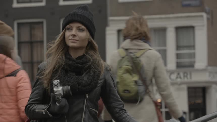 A woman walks down a city street with a camera