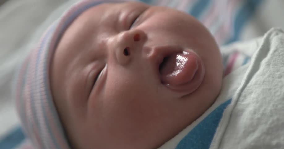 A tiny newborn baby sticks their tongue out