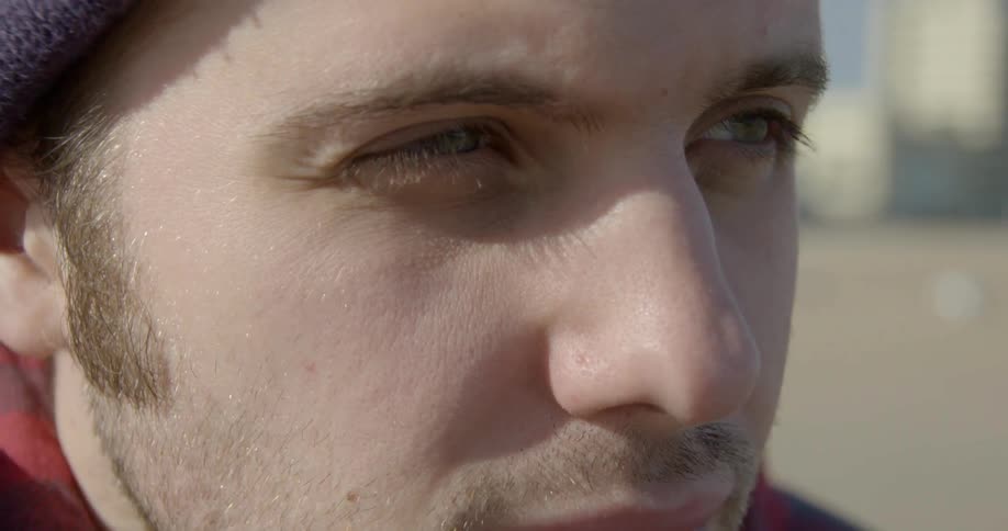 An unshaven, brunette man who is watching something on a chilly, sunny day