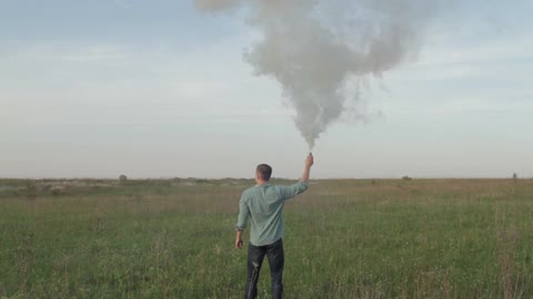 A man lights a flare during the day while standing in a field