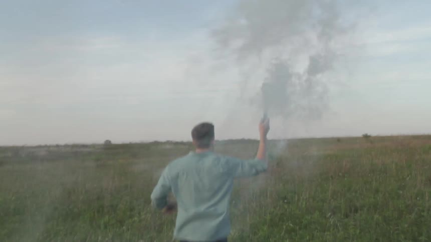 A man runs through a field with a smoking object