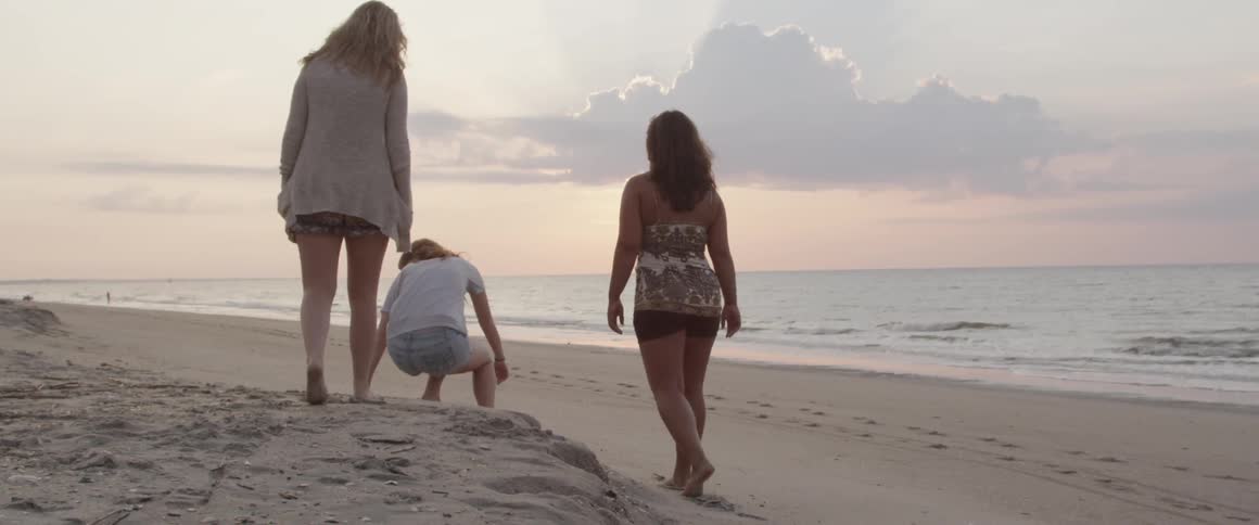 Three women walk on the beach at sunset