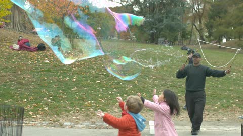 A large bubble flows through the air with children chasing after it
