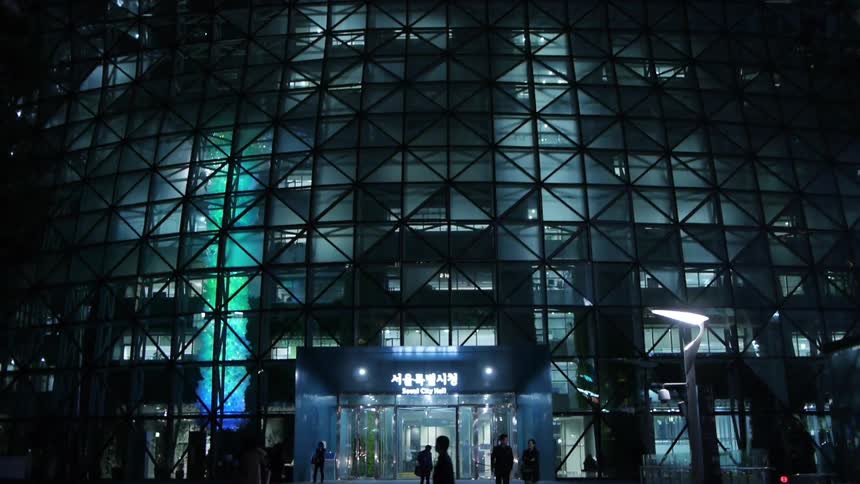 A building is lit up at night while people walk past