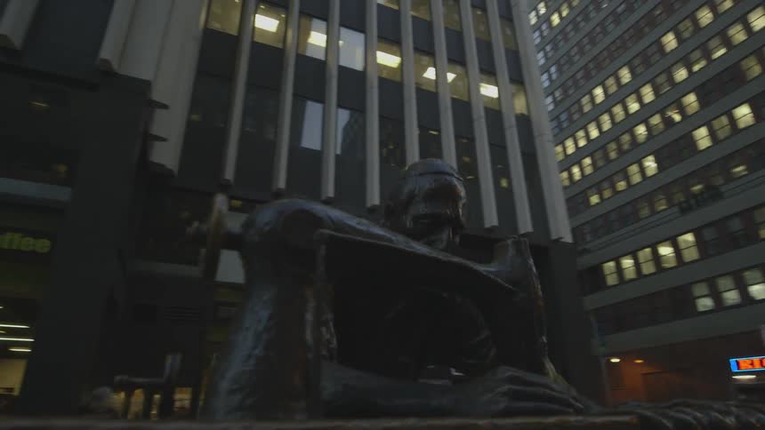 A statue of a man with a sewing machine is shown in the city