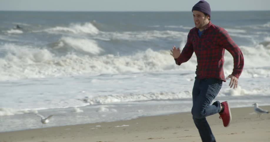 A man runs on the beach while birds fly around him
