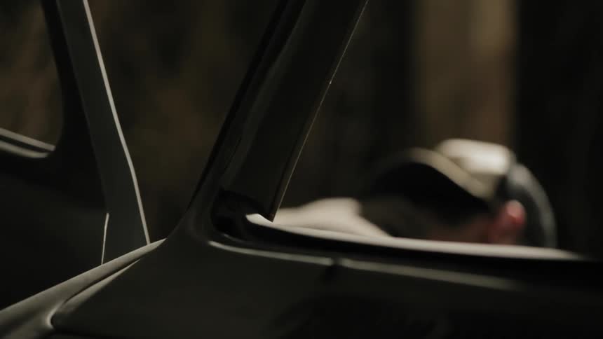 A man in a baseball cap is doing something behind an open car door
