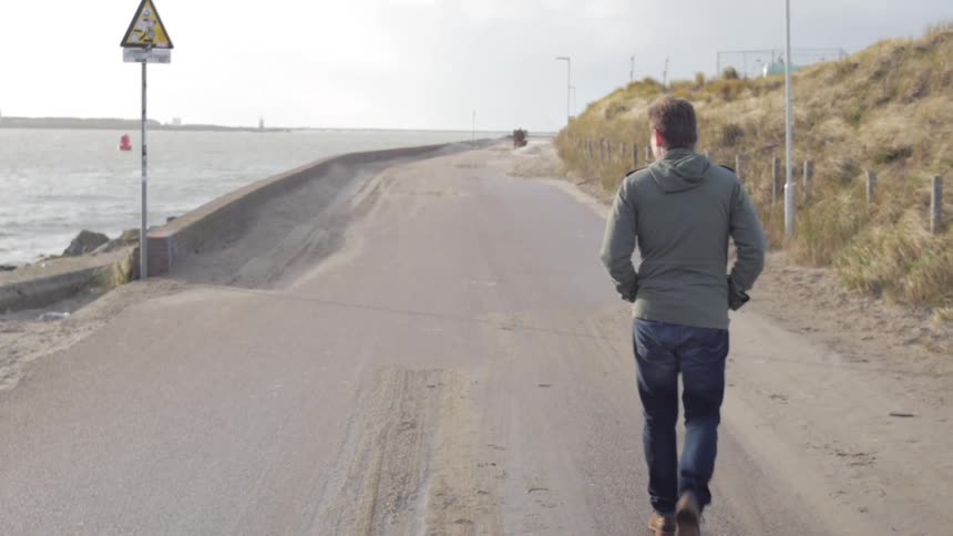 A man walks down a road near the beach