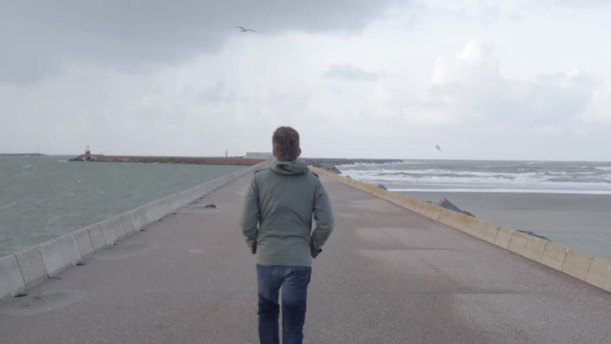 A man walking on a lonely bridge laid across the sea