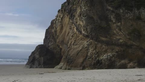 Waves crashing in the background with a giant rock in the foreground at a beach with the ocean on a cloudy day