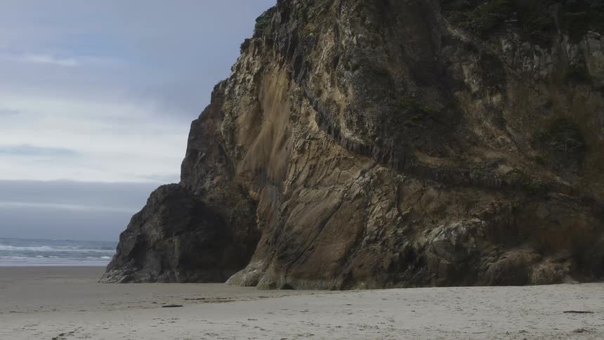 Waves crashing in the background with a giant rock in the foreground at a beach with the ocean on a cloudy day