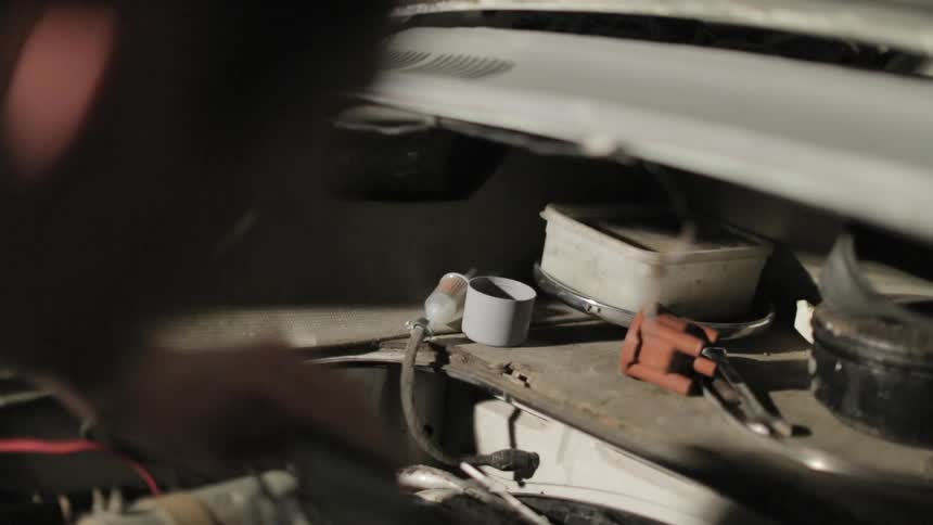 Man looking for a tool under the hood of a car
