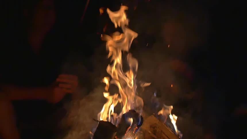 Two people sit in front of a campfire at night, about to roast marshmallows