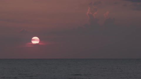 Waves rippling as the sun sets in a cloudy sky