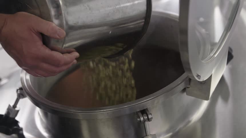 Person pouring seeds into a large, steaming canister