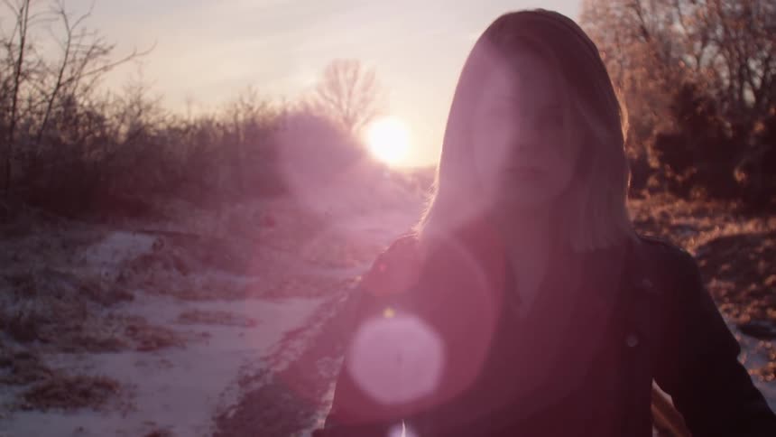 A woman is standing with the sunset behind her