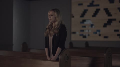 A woman walks up to the pews in a church and stands facing forward