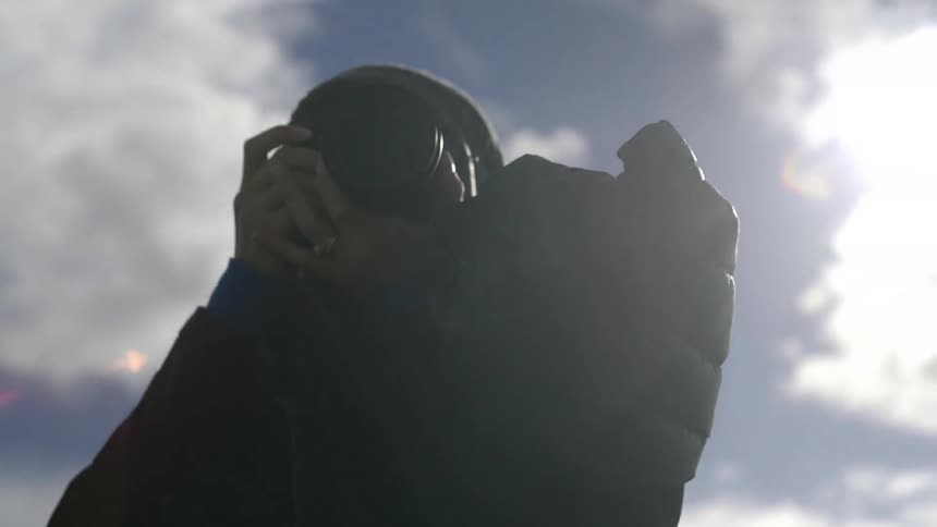 Young, blonde woman taking photographs on a cold, partially cloudy day