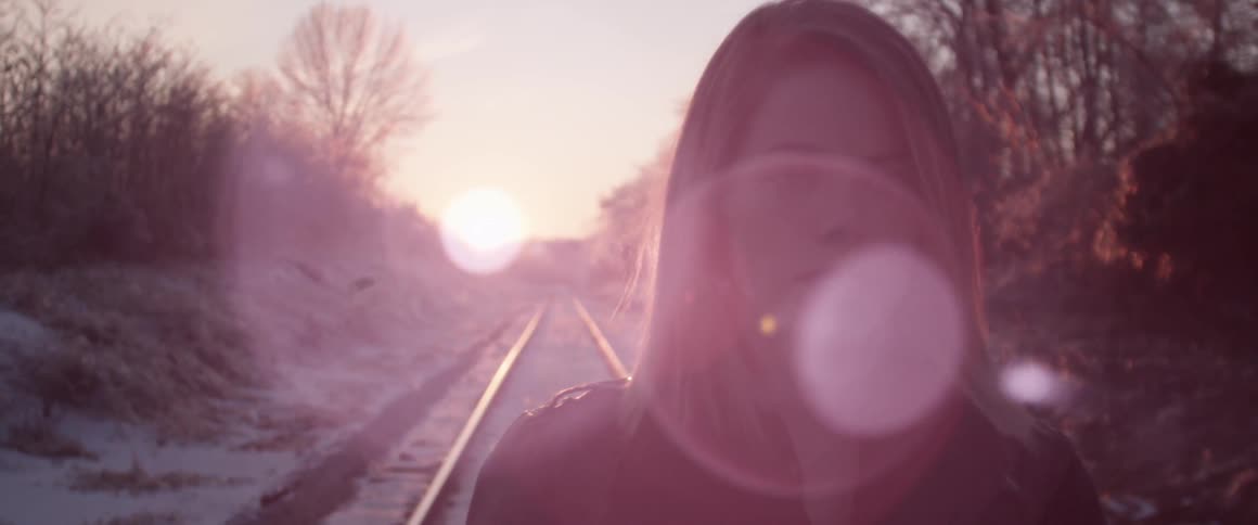 A woman stands on a railroad track at sunset