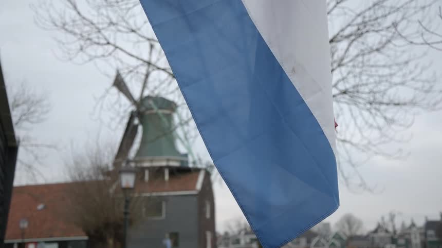 A flag billows in the wind with a windmill in the background