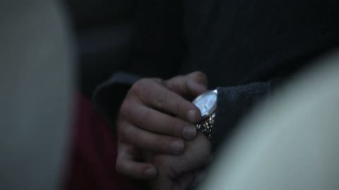 A man is rubbing something off of his watch, then rubs his fingers together