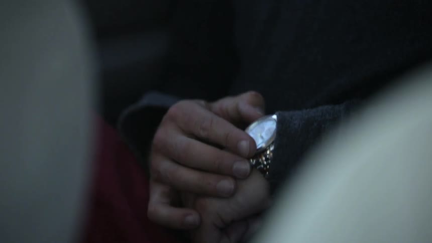 A man is rubbing something off of his watch, then rubs his fingers together