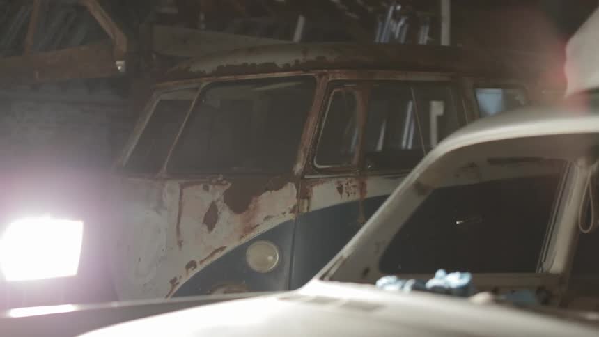 A light shines brightly on wrecked cars including a rusted out van