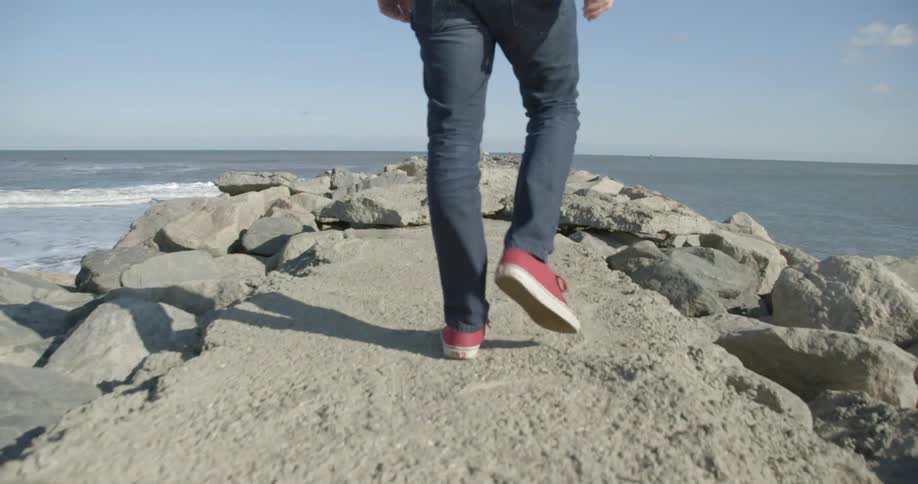 A man walks on a pile of boulders and towards the ocean